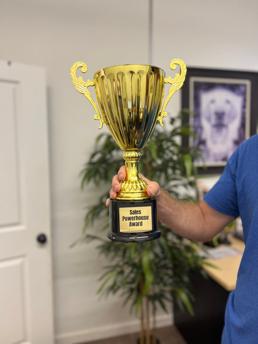 A man holds an extra large gold custom engraved trophy award cup.